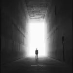 Czarno-biała fotografia artystyczna przedstawiająca sylwetkę człowieka stojącą w ciemności naprzeciw oślepiającego światła, symbol zmartwychwstania i życia wiecznego inspirowany Ewangelią Łukasza 20