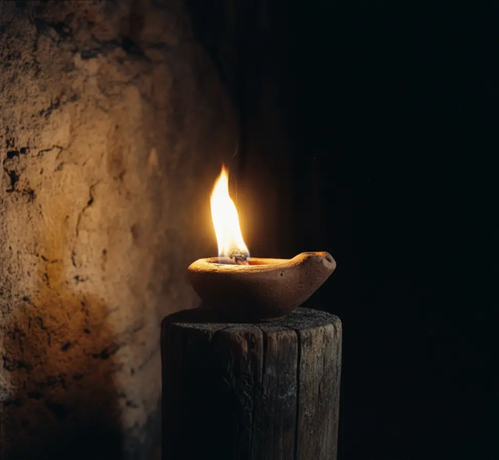 Zapalona biblijna lampa oliwna na świeczniku rozświetlająca mrok symbolizująca żywą wiarę.